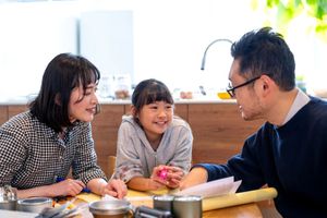 防災用品が並べられた机に集まって楽しそうな雰囲気を作りながら防災会議を行う三人家族