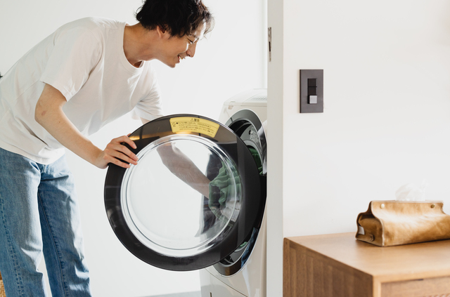  ドラム式洗濯機に洗濯物を入れる男性